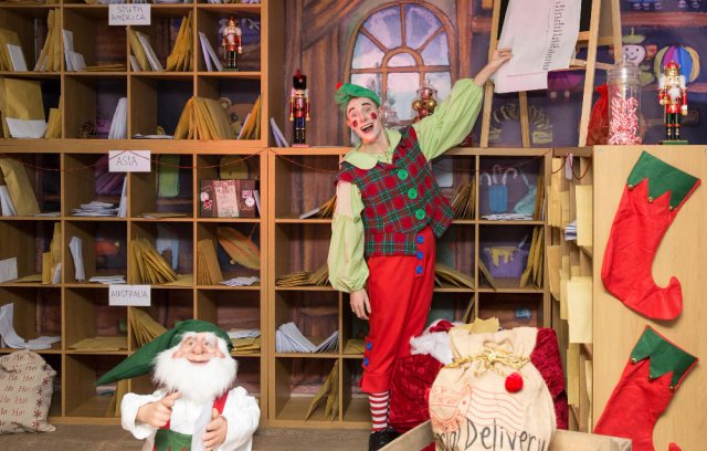 Santa's Elf stood in front of a childs christmas list. The image also features letters, a gonk and red stockings.