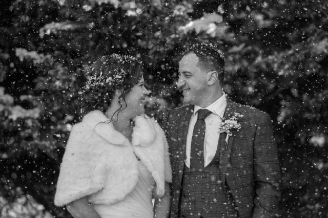 a man and woman stand in the artificial snow on their wedding day